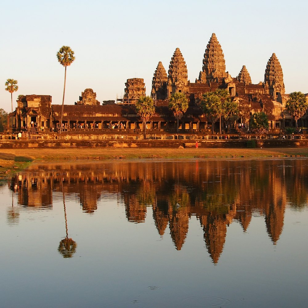 A temple's towers reflected in still water at sunrise.